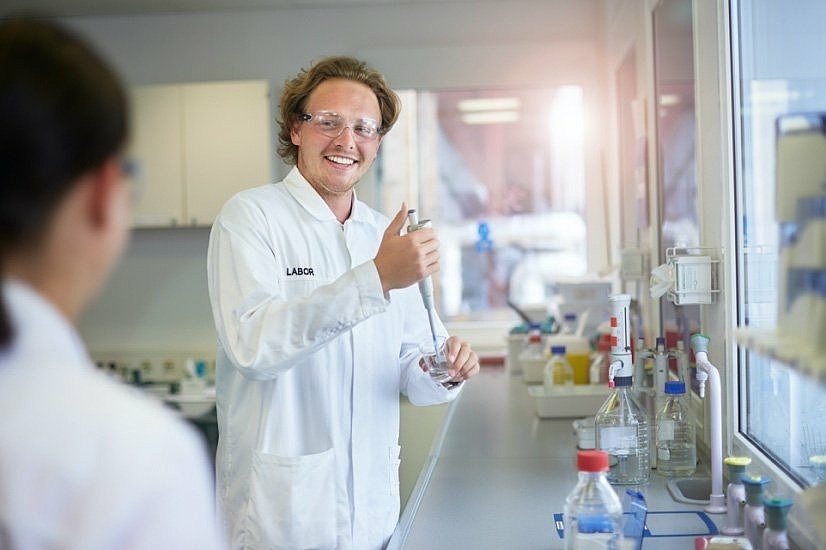 Ein Mitarbeiter in Laborkeidung der im Labor eine Flüssigkeit in ein Glas spritzt 