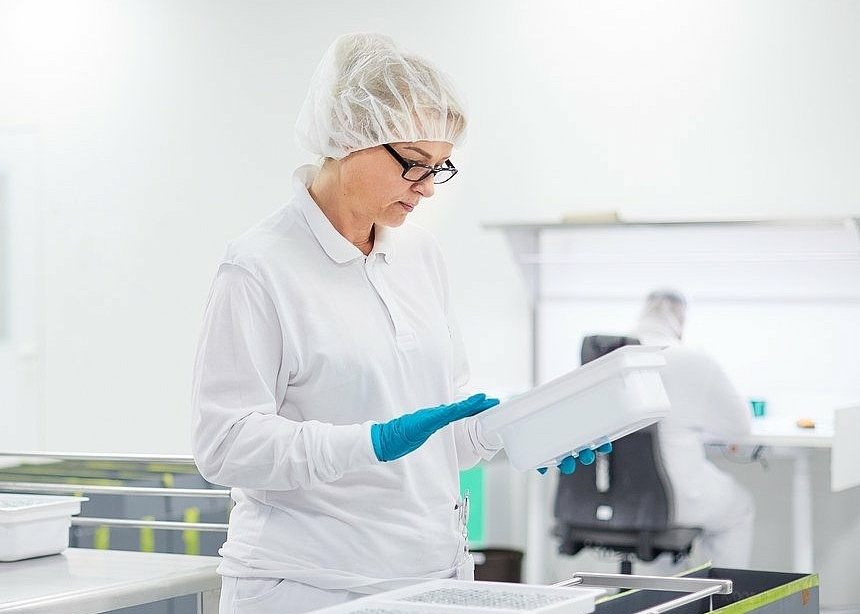 Mitarbeiterin in Laborkleidung in der optischen Kontrolle die eine Box in der Hand hält 