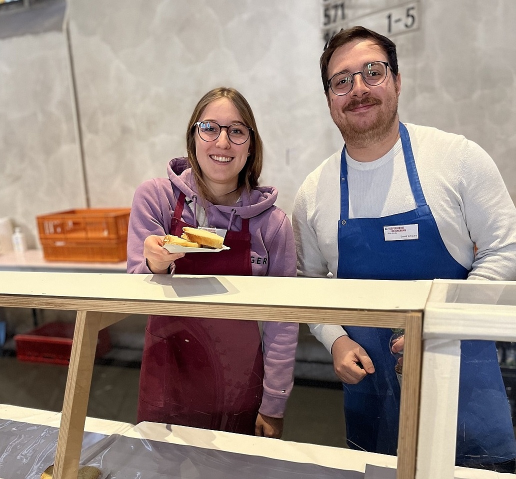 Eine Auszubildende und ein Ausbilder die zusammen in der Vesperkirche Kuchen verkaufen  